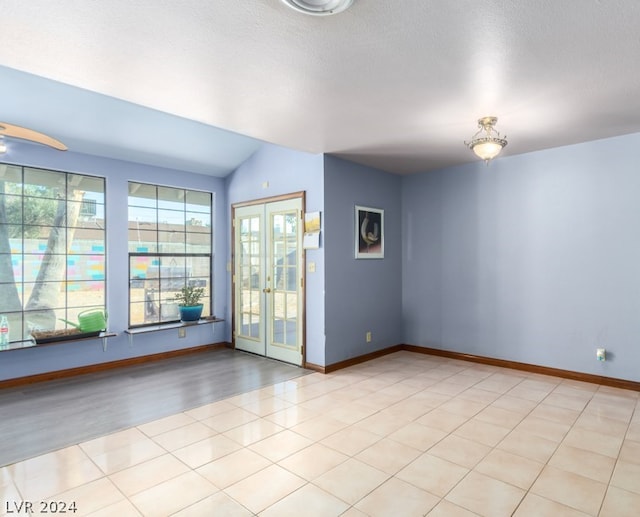 tiled spare room featuring vaulted ceiling, a textured ceiling, and french doors