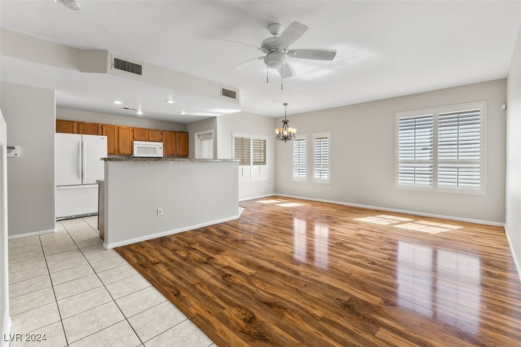 unfurnished living room featuring ceiling fan with notable chandelier and light hardwood / wood-style floors