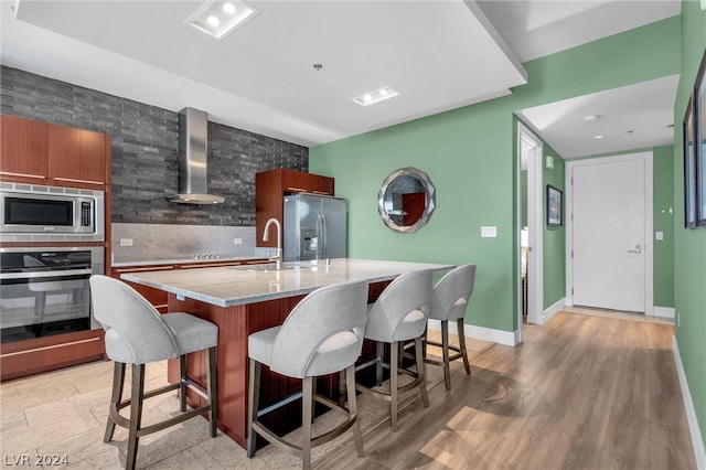 kitchen featuring wall chimney exhaust hood, light hardwood / wood-style floors, a breakfast bar area, and appliances with stainless steel finishes