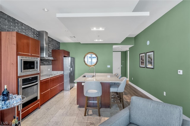 kitchen featuring a kitchen breakfast bar, appliances with stainless steel finishes, wall chimney exhaust hood, sink, and tasteful backsplash