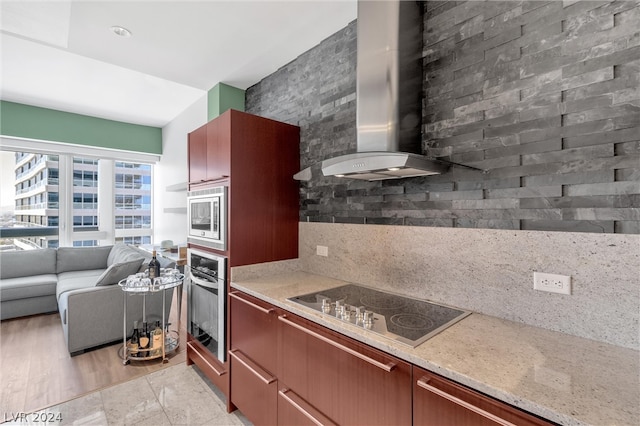 kitchen featuring wall chimney range hood, light stone countertops, light tile flooring, and appliances with stainless steel finishes