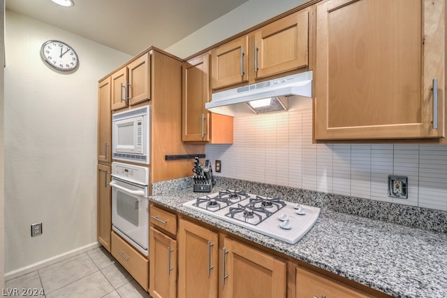 kitchen with dark stone countertops, light tile floors, white appliances, and backsplash