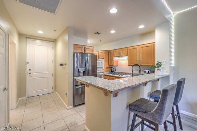 kitchen featuring kitchen peninsula, a breakfast bar area, light stone countertops, appliances with stainless steel finishes, and light tile floors