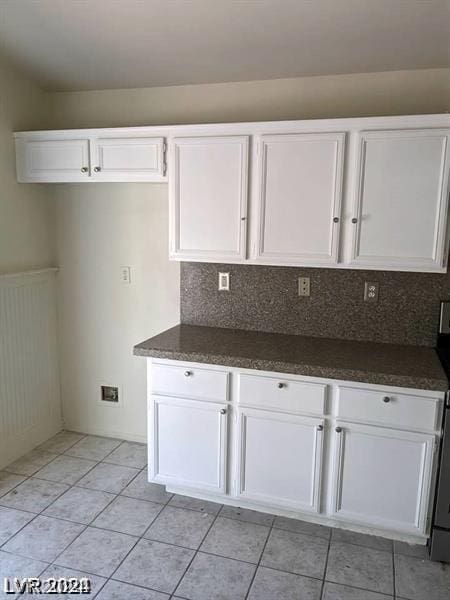 kitchen featuring white cabinets, light tile patterned floors, tasteful backsplash, and dark stone counters