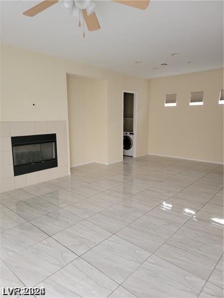 unfurnished living room with a tiled fireplace, washer / clothes dryer, and ceiling fan