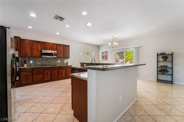 kitchen with dark stone countertops, stainless steel appliances, a center island with sink, and light tile patterned floors