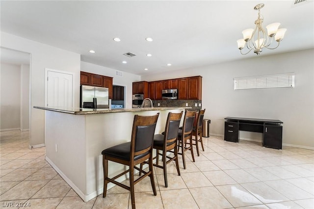 kitchen featuring light tile patterned floors, backsplash, stainless steel appliances, light stone counters, and a kitchen bar