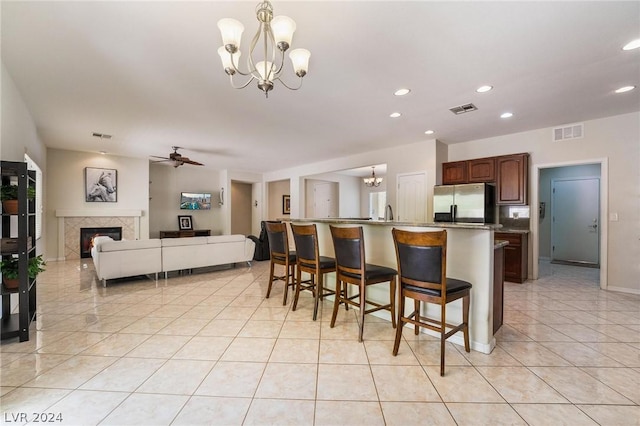 kitchen featuring pendant lighting, a tile fireplace, a kitchen breakfast bar, stainless steel refrigerator with ice dispenser, and an island with sink