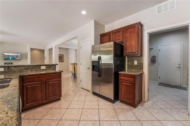 kitchen with light tile patterned floors, sink, dark stone countertops, backsplash, and stainless steel refrigerator with ice dispenser