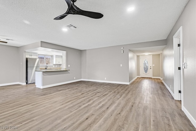 unfurnished living room featuring a textured ceiling, ceiling fan, light hardwood / wood-style floors, and sink