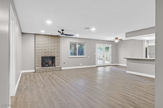 unfurnished living room with ceiling fan, french doors, a brick fireplace, hardwood / wood-style floors, and a textured ceiling