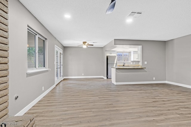 unfurnished living room with a textured ceiling, light hardwood / wood-style flooring, ceiling fan, and sink