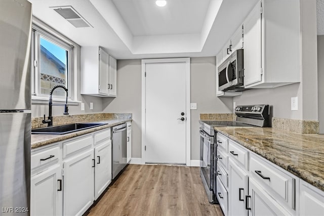 kitchen featuring stainless steel appliances, a raised ceiling, sink, white cabinets, and light hardwood / wood-style floors