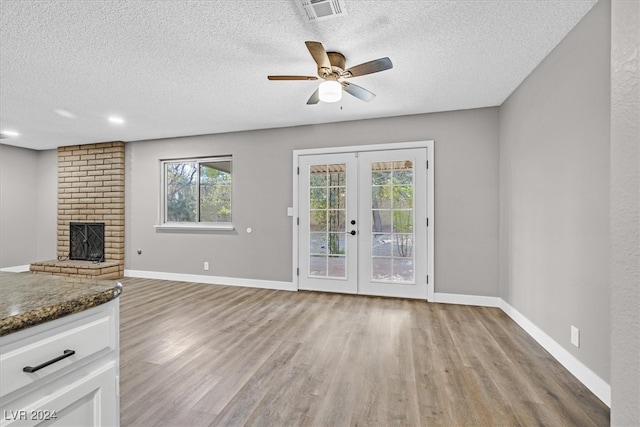 unfurnished living room with a fireplace, light wood-type flooring, a textured ceiling, and french doors