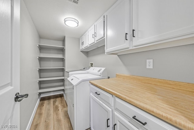 washroom with cabinets, washing machine and dryer, and light hardwood / wood-style floors