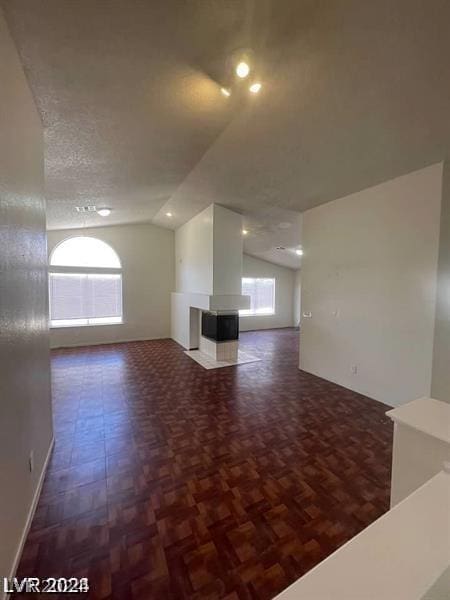 unfurnished living room with a textured ceiling, dark parquet flooring, a healthy amount of sunlight, and lofted ceiling