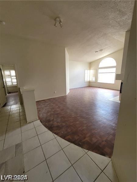 empty room featuring a textured ceiling, vaulted ceiling, a wealth of natural light, and light tile patterned flooring