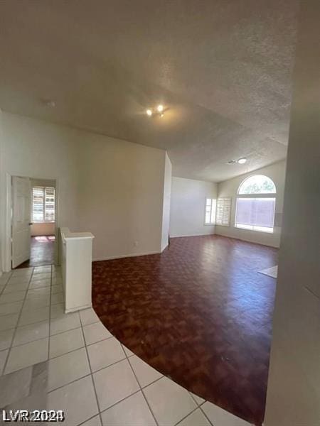 unfurnished room with plenty of natural light, light tile patterned floors, a textured ceiling, and vaulted ceiling