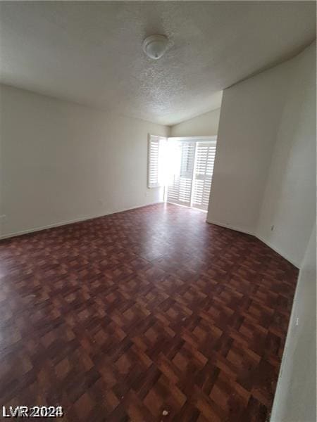 unfurnished room featuring vaulted ceiling, dark parquet floors, and a textured ceiling