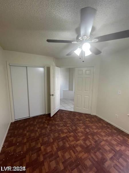 unfurnished bedroom with parquet floors, a textured ceiling, a closet, and ceiling fan