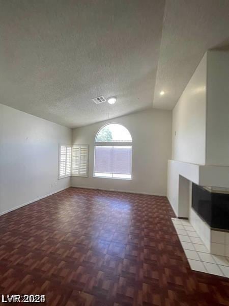 unfurnished living room with a textured ceiling, vaulted ceiling, parquet floors, and a tiled fireplace