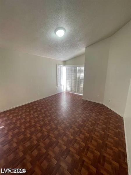 spare room with dark parquet flooring, a textured ceiling, and vaulted ceiling