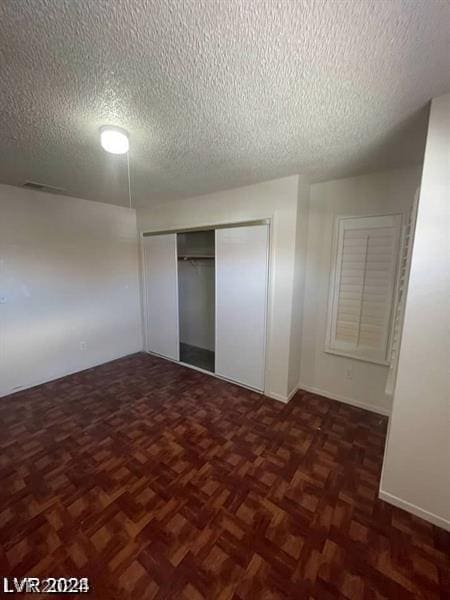 unfurnished bedroom with dark parquet floors, a textured ceiling, and a closet