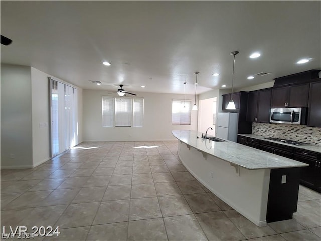 kitchen with light stone countertops, white fridge, ceiling fan, and an island with sink