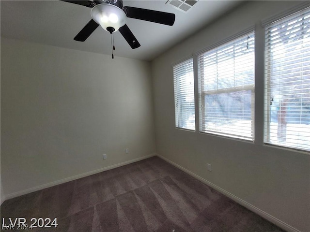 empty room featuring ceiling fan, a healthy amount of sunlight, and dark colored carpet