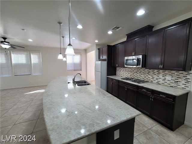 kitchen featuring a center island with sink, sink, hanging light fixtures, appliances with stainless steel finishes, and light stone counters