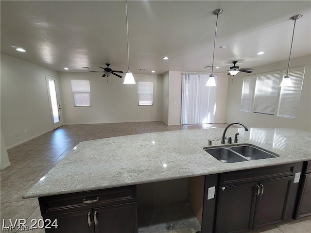 kitchen with a center island with sink, sink, ceiling fan, light stone countertops, and light tile patterned flooring