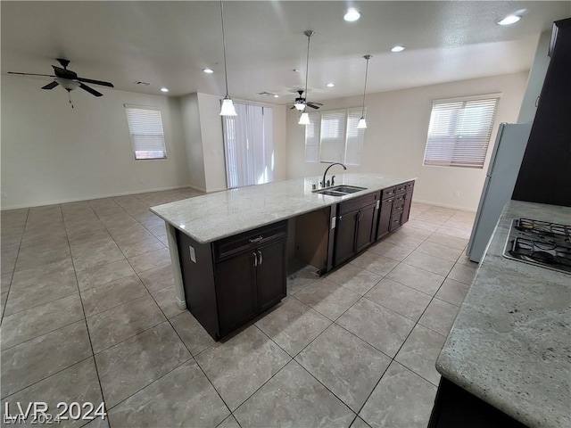 kitchen featuring a center island with sink, light stone counters, hanging light fixtures, and sink