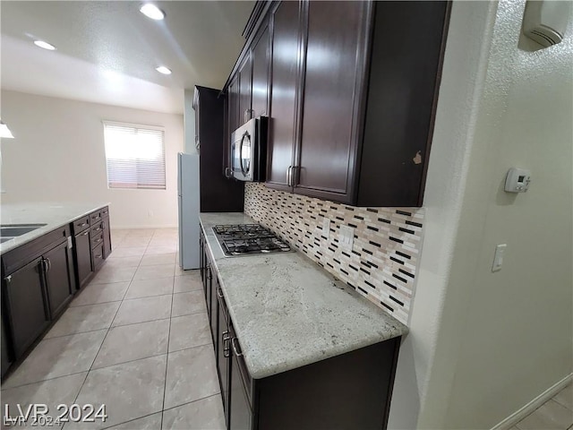 kitchen with tasteful backsplash, light stone countertops, light tile patterned flooring, and stainless steel appliances