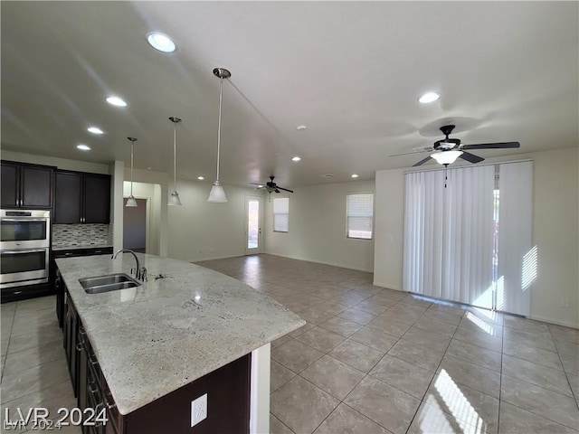 kitchen featuring backsplash, a center island with sink, sink, decorative light fixtures, and stainless steel double oven