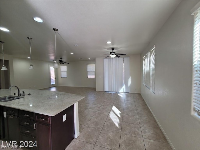 kitchen with light stone countertops, pendant lighting, ceiling fan, and sink