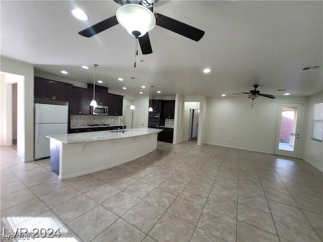 kitchen featuring tasteful backsplash, white fridge, an island with sink, and light tile patterned floors