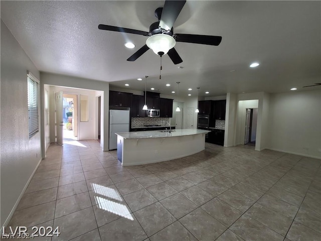 kitchen featuring appliances with stainless steel finishes, tasteful backsplash, ceiling fan, a center island with sink, and light tile patterned flooring