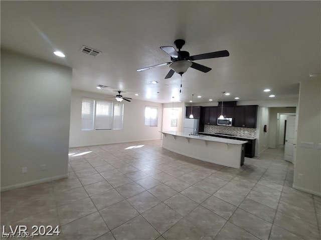 kitchen with backsplash, a center island with sink, ceiling fan, light tile patterned flooring, and a kitchen bar