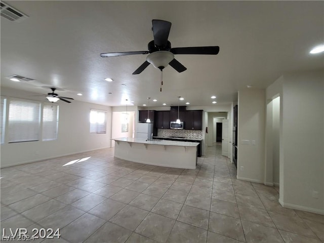 kitchen with ceiling fan, light tile patterned floors, an island with sink, tasteful backsplash, and a breakfast bar area