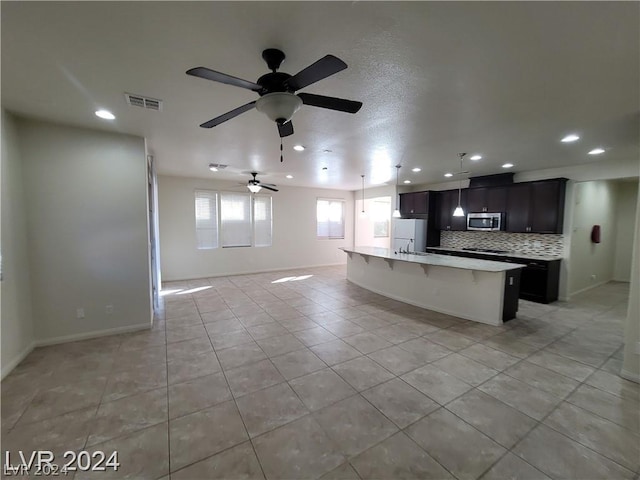 kitchen with a kitchen island with sink, a kitchen breakfast bar, white fridge, decorative backsplash, and light tile patterned flooring