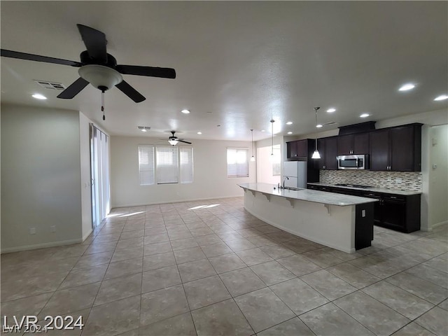 kitchen featuring backsplash, ceiling fan, sink, light tile patterned floors, and an island with sink