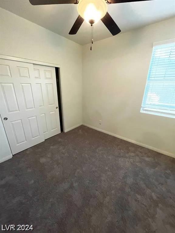 unfurnished bedroom featuring ceiling fan, dark carpet, and a closet