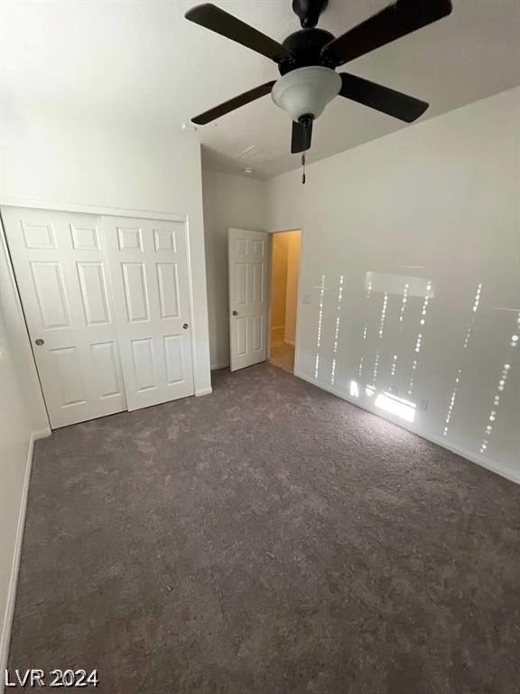 unfurnished bedroom with dark colored carpet, ceiling fan, and a closet