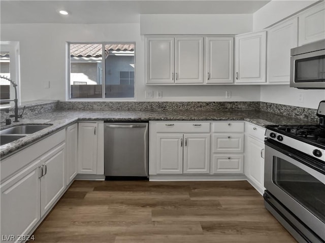 kitchen with sink, dark stone countertops, white cabinetry, wood-type flooring, and stainless steel appliances