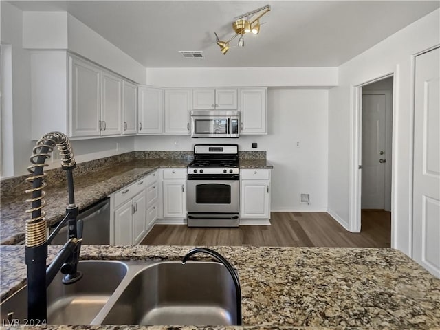 kitchen with sink, dark hardwood / wood-style floors, dark stone countertops, white cabinets, and appliances with stainless steel finishes