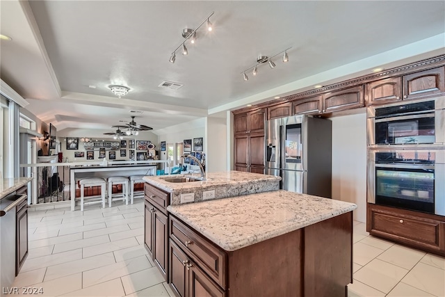 kitchen featuring a center island with sink, sink, light stone countertops, ceiling fan, and stainless steel fridge with ice dispenser