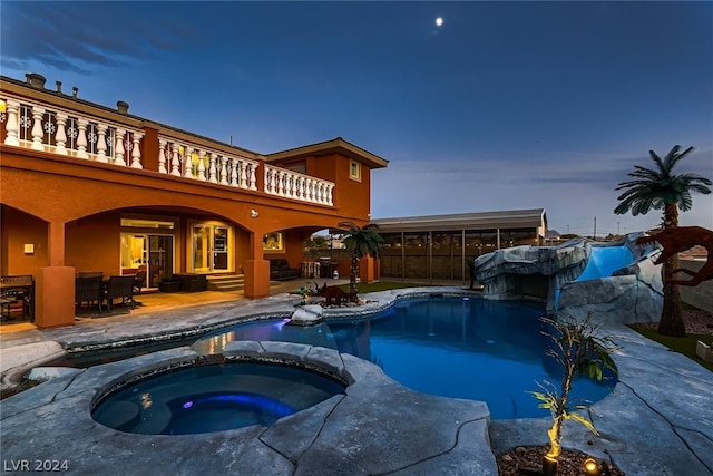 pool at dusk with a patio and an in ground hot tub