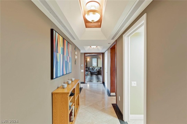 corridor with light tile patterned floors and a raised ceiling