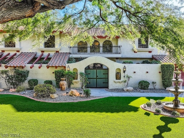 rear view of house with a balcony, a tiled roof, a yard, and stucco siding