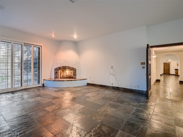 unfurnished living room with stone tile floors, arched walkways, a fireplace, and baseboards